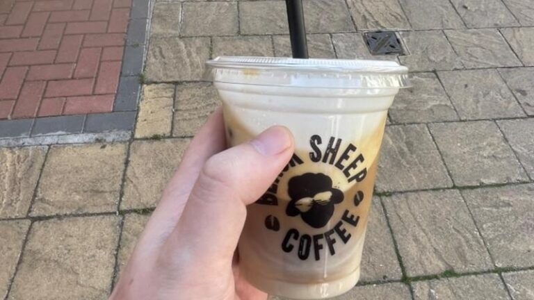 Hand holding a Black Sheep Coffee Oatly Cold Foam Iced Latte while walking in Colchester town centre