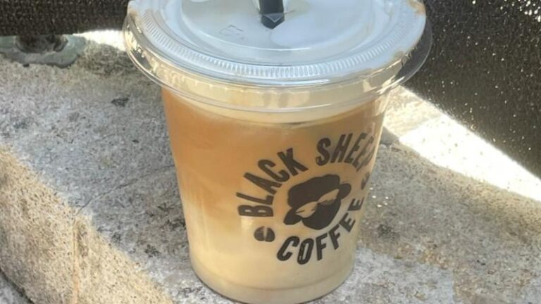 Black Sheep Coffee Oatly Cold Foam Iced Latte placed on a stone ledge outdoors