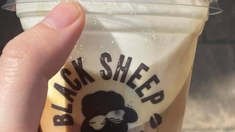 Hand holding the Black Sheep Coffee Oatly Cold Foam Iced Latte close to the camera