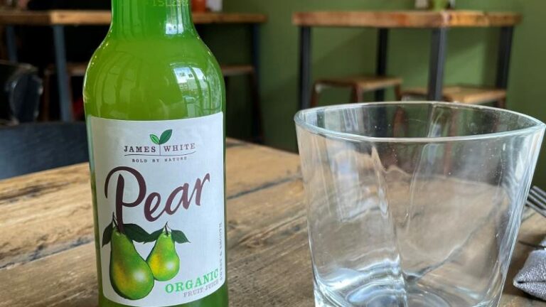 Bottle of James White organic pear juice with an empty glass at Cradle in Sudbury