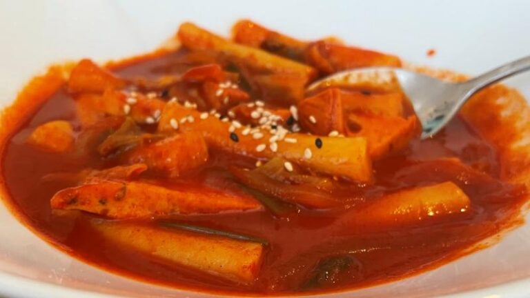 Close-up shot of vegan Spicy Rice Cakes (Tteokbokki) in red sauce with a spoon in the dish at MukBap in London