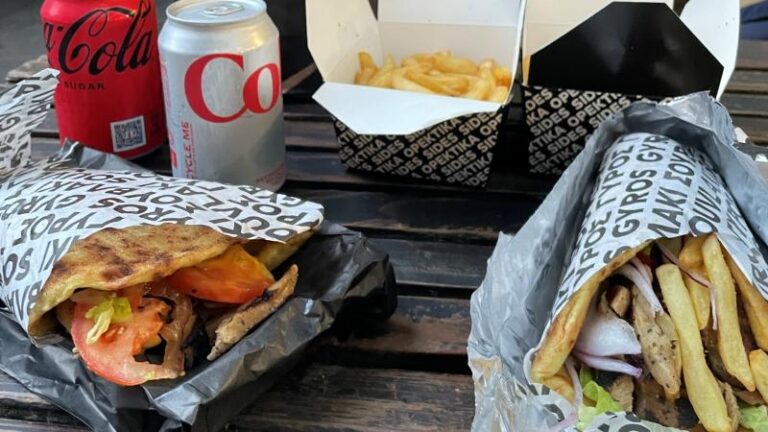 Picture of two vegan gyros wraps, two boxes of vegan oregano fries, one Diet Coke and one Coca-Cola on a bench from The Athenian