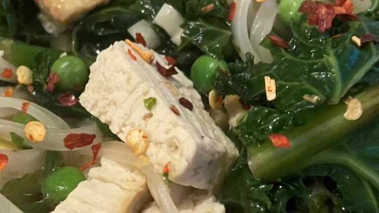 Very close-up of tofu and kale in homemade ramen soup with chilli flakes